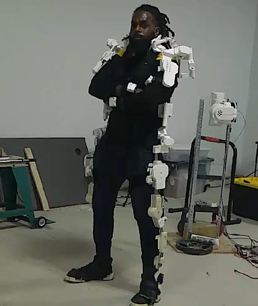 Man wearing a robotic exoskeleton suit in a workshop, showcasing wearable robotics innovation.